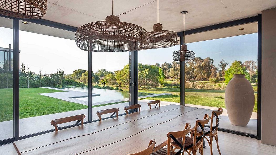 Modern rustic dining room with large woven pendant lights, wooden table, and panoramic view of lush garden.