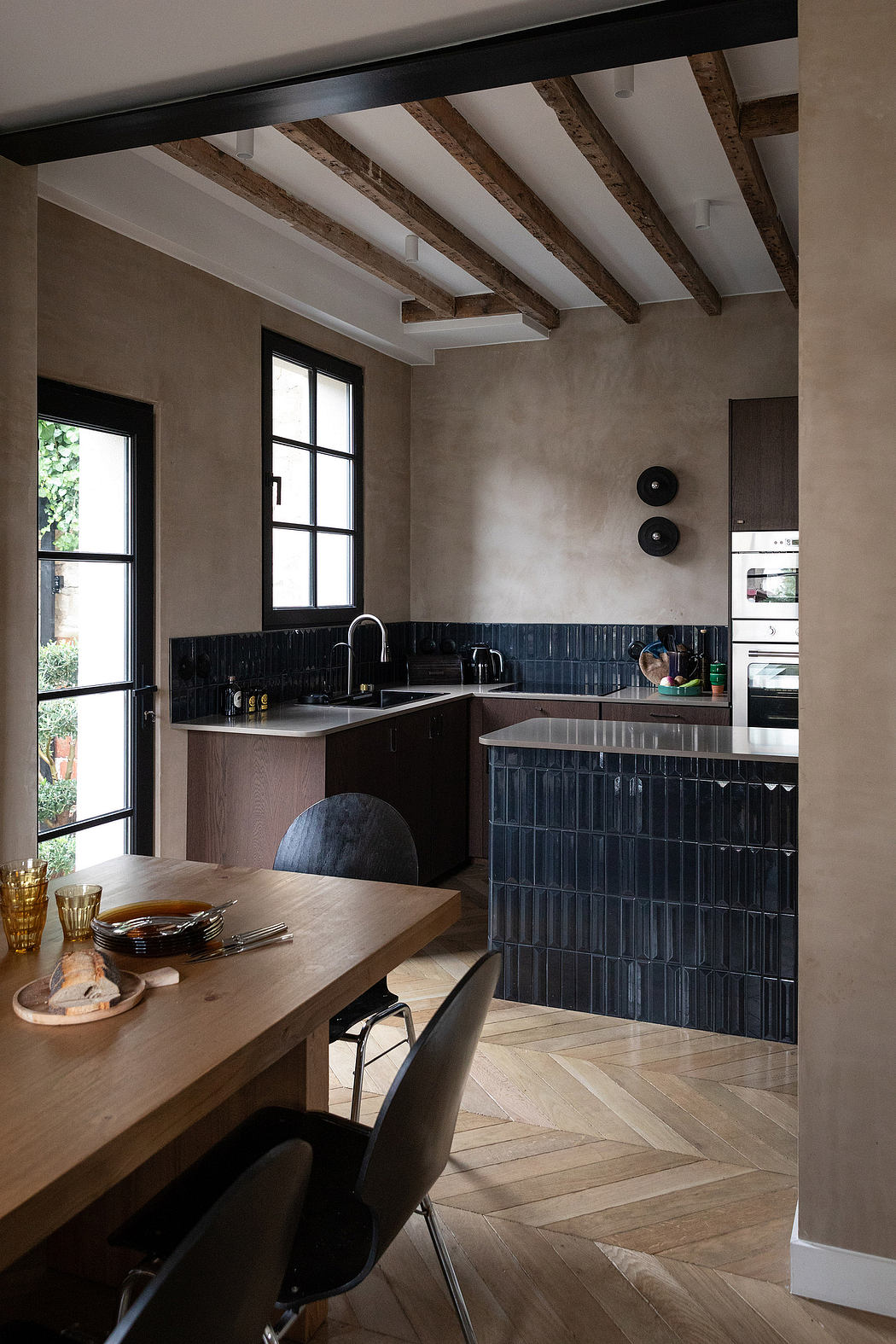 A modern kitchen with exposed wooden beams, dark tiles, and a wooden dining table.