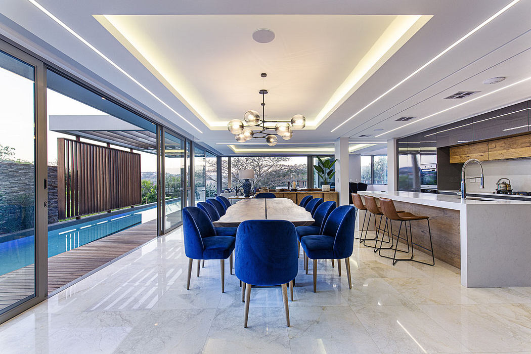 Spacious, open-plan living area with a modern chandelier, plush blue seating, and a view of the pool.