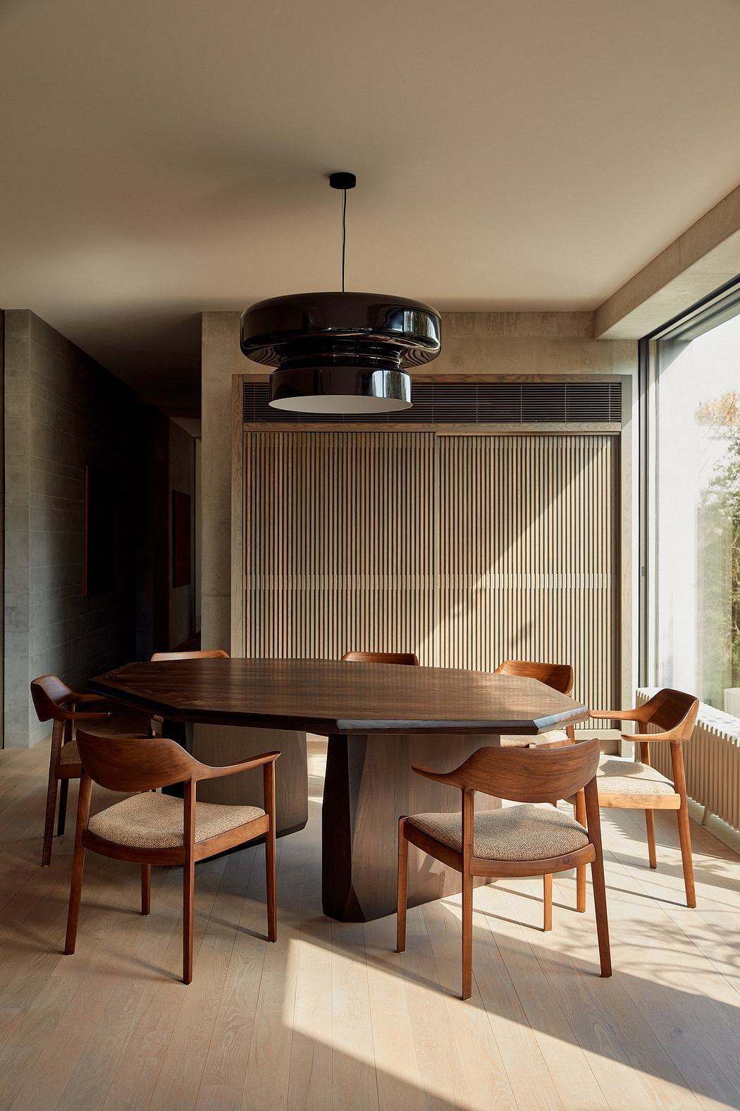 A modern dining space with a sleek wooden table, plush chairs, and a striking pendant light.