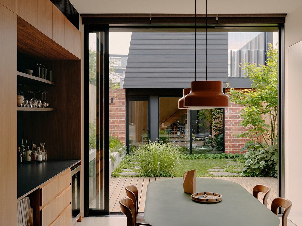 A modern, open-plan dining room with large windows overlooking a lush garden and outdoor seating area.