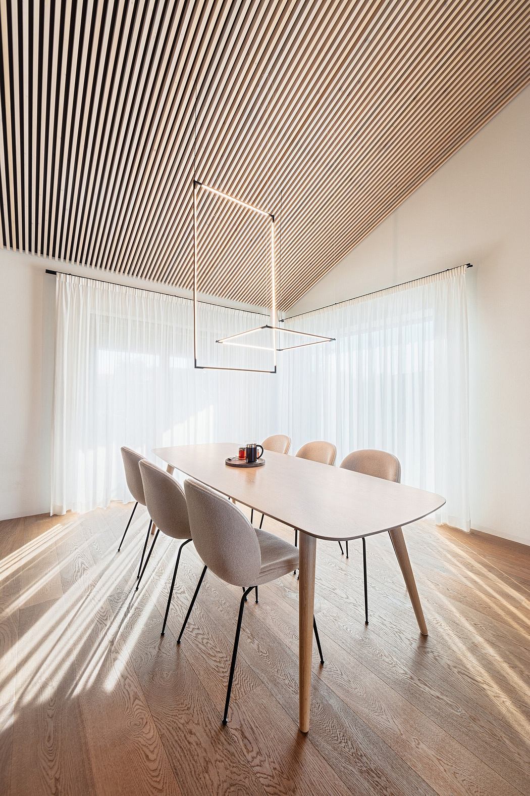 A modern dining room with a minimalist geometric light fixture and striped wood ceiling.