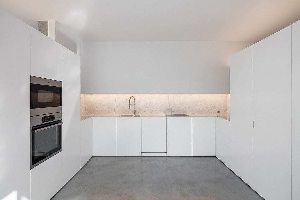 Minimalist kitchen design with sleek white cabinets, marble backsplash, and concrete floors.
