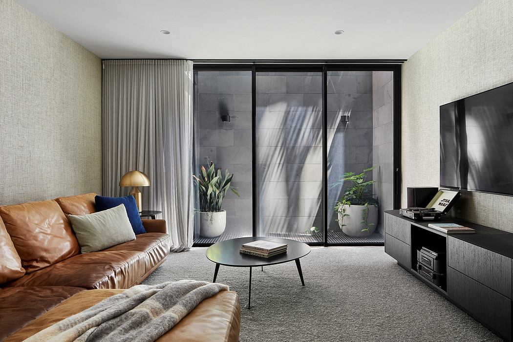 Modern living room with leather sofa, coffee table, and large windows overlooking greenery.