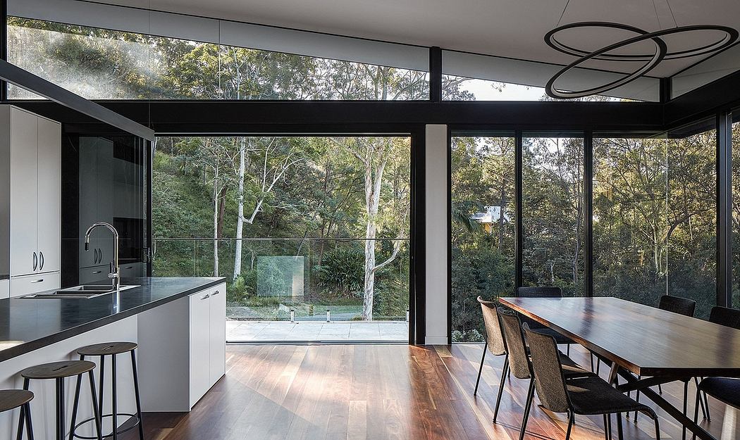 Modern kitchen and dining room with glass walls overlooking lush greenery.