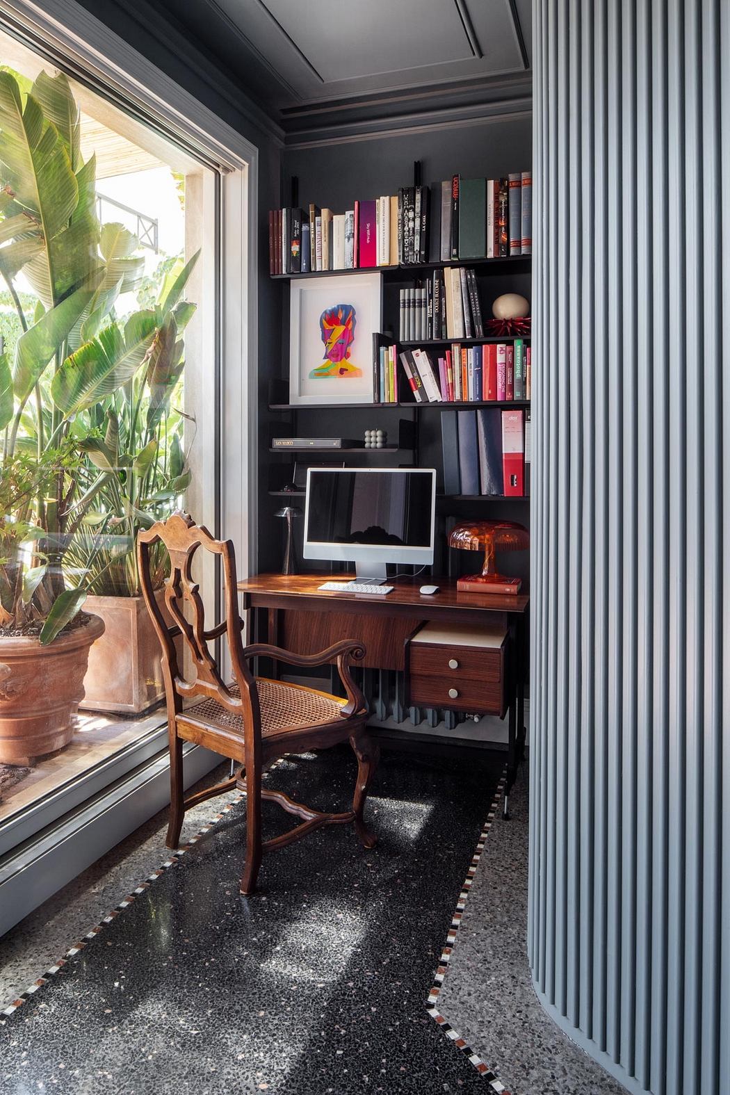 A cozy home office nook with built-in bookshelves, a vintage desk, and tropical foliage.
