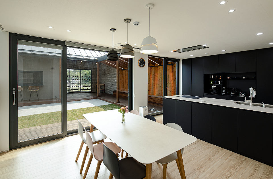 Modern kitchen with black cabinets, large windows, and a dining table overlooking a garden.