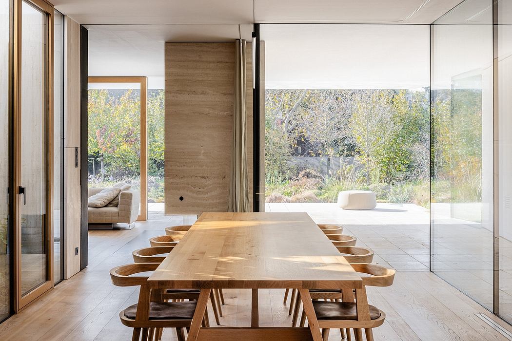 Large wooden dining table surrounded by chairs in minimalist interior with nature view.