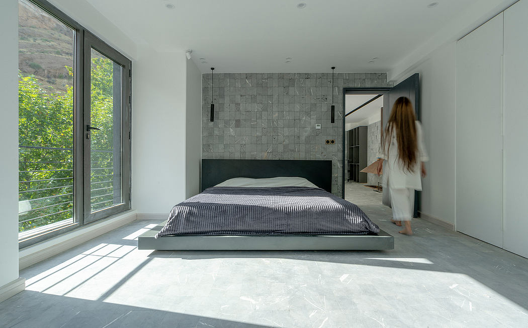 Large open-plan bedroom with minimalist decor, gray tile accent wall, and expansive windows.