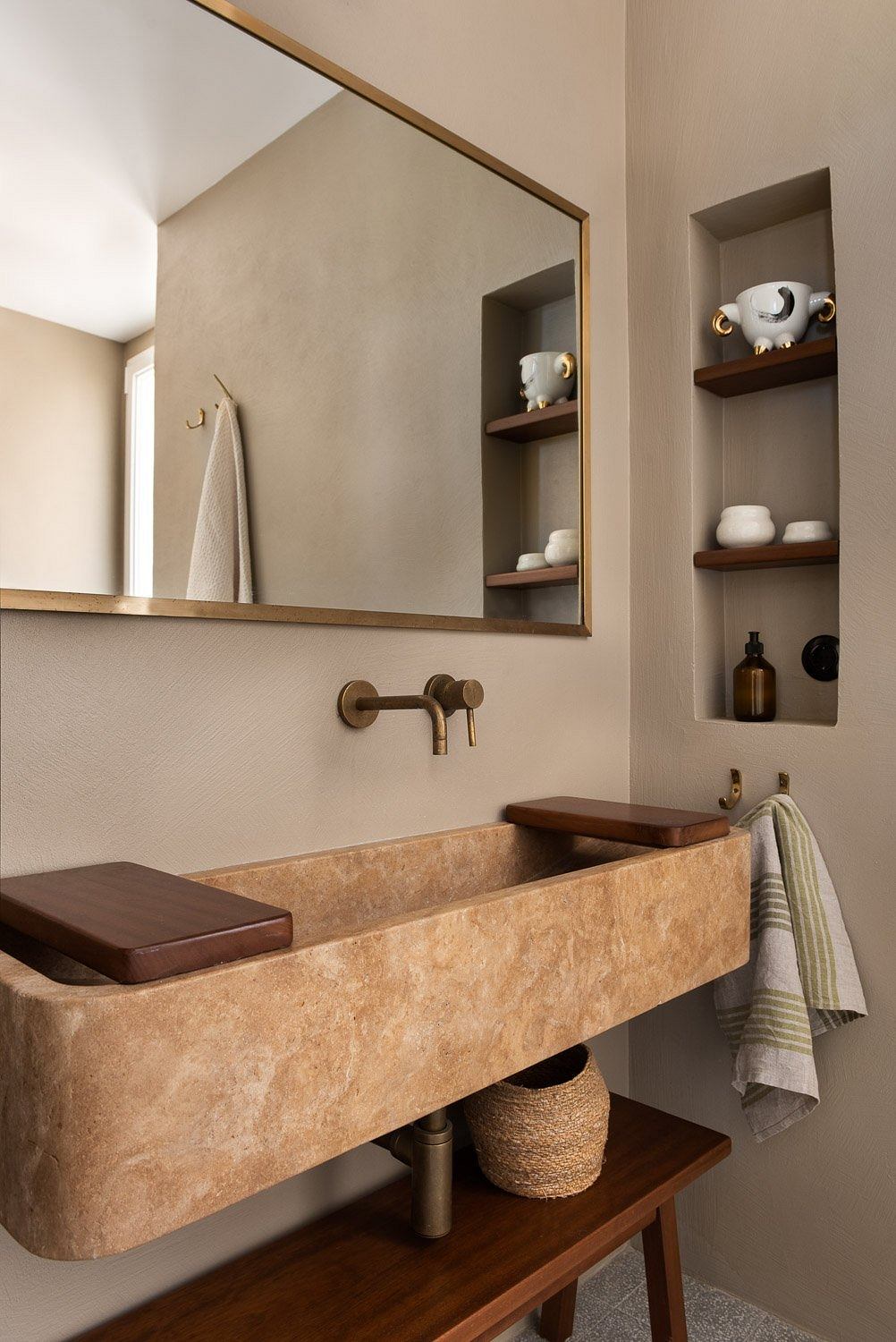 A warm, contemporary bathroom with a stone sink, shelves, and a large mirror.