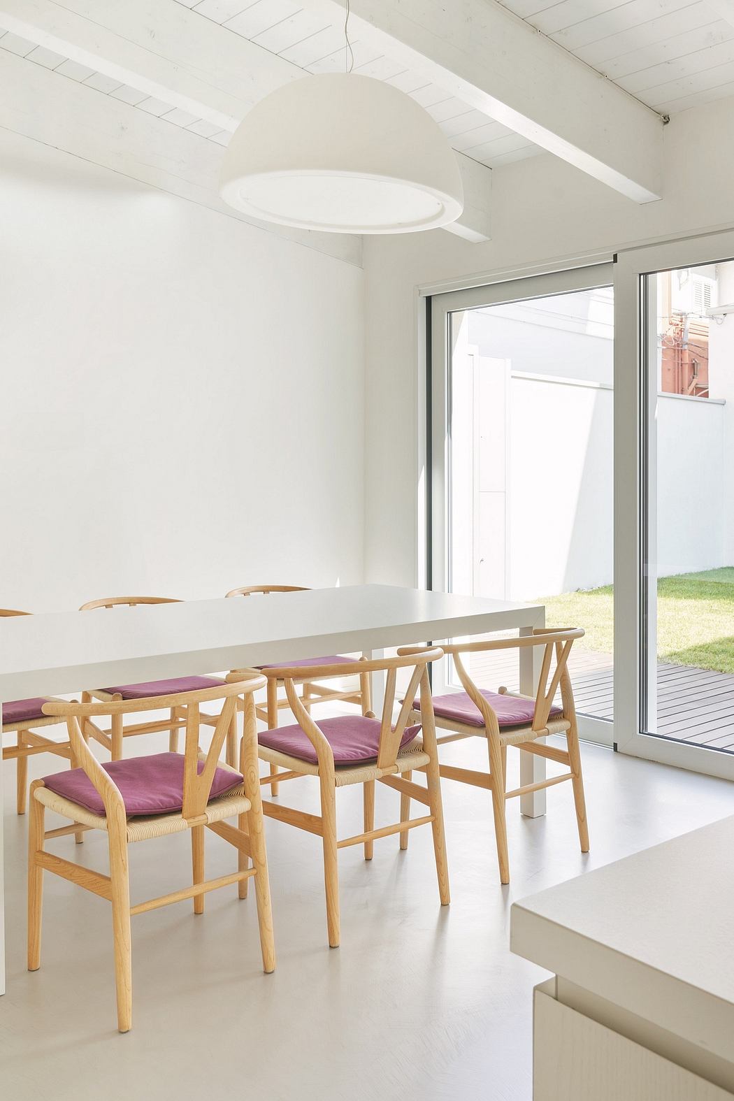 Minimalist dining room with large white pendant light, wooden chairs, and sliding glass doors.