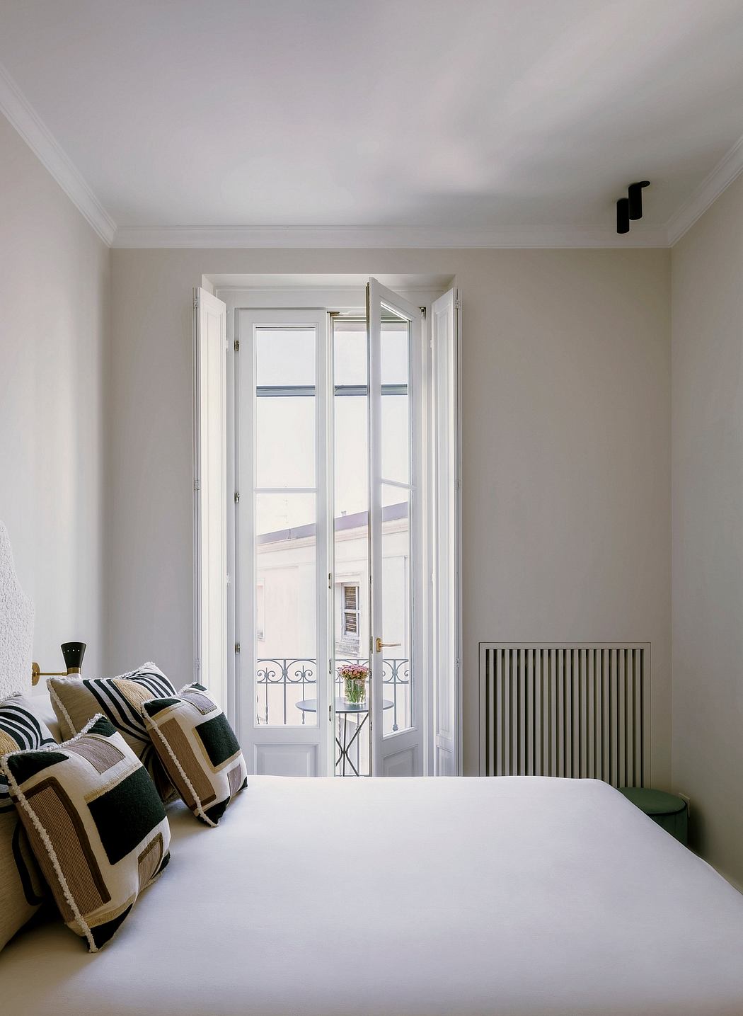 A cozy bedroom with white walls, wooden floors, and a large window overlooking a balcony.