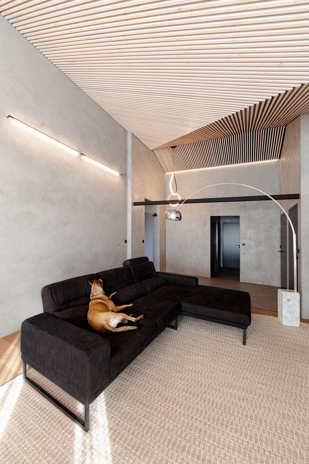 Minimalist living room with wood-paneled ceiling, dark sofa, and textured floor.