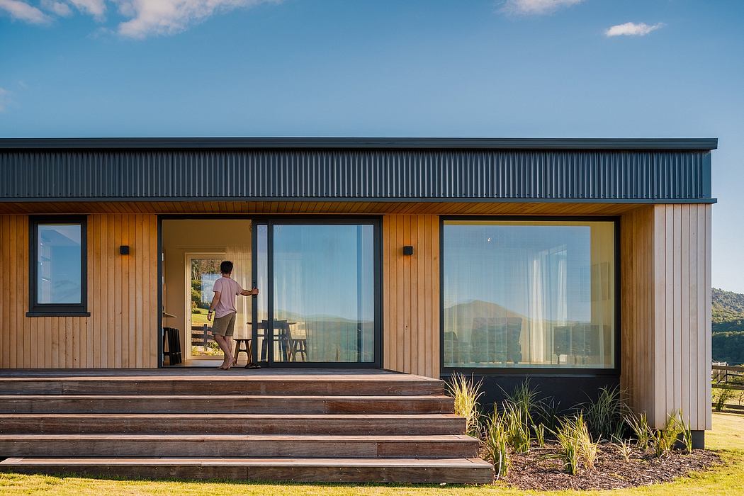 Modern wooden cabin with large windows, deck, and steps leading to the entrance.