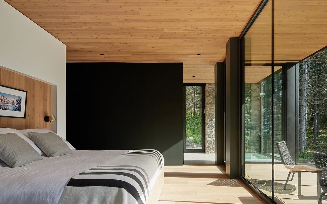 A cozy wooden bedroom with large glass windows overlooking a lush, forested landscape.