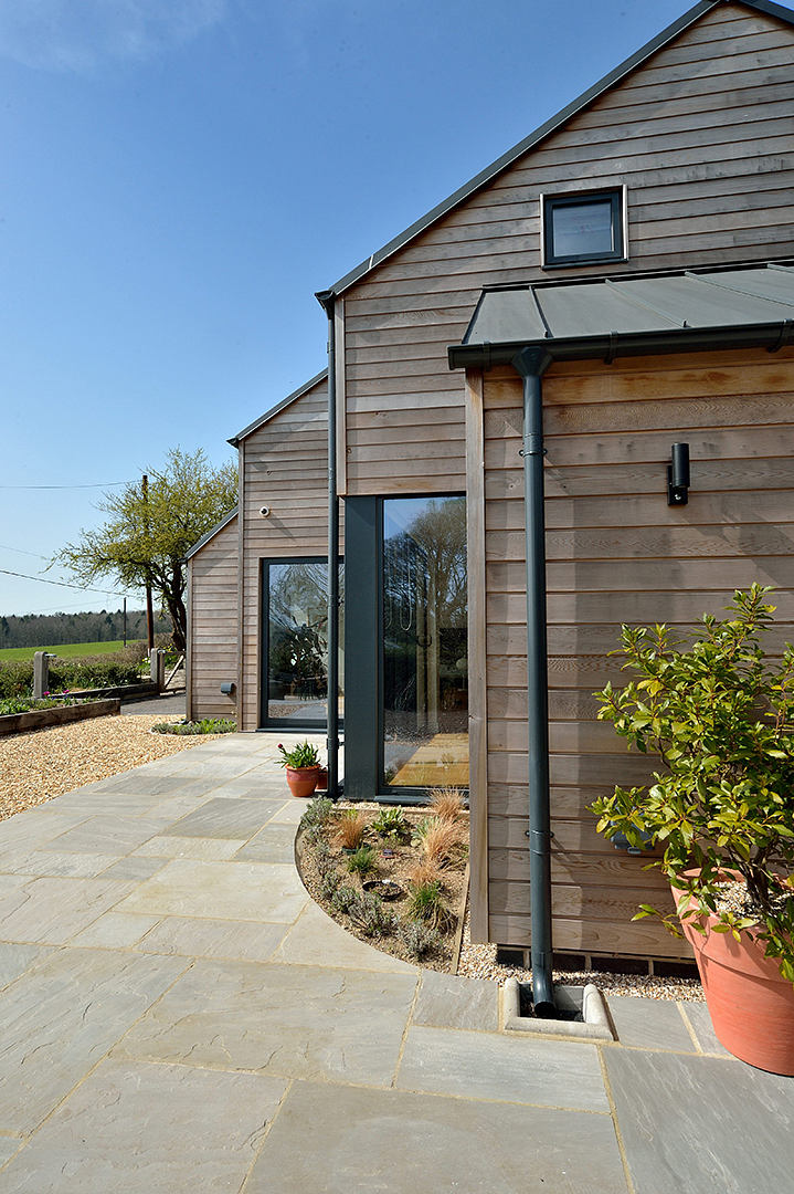 A modern, wooden-clad house with an attractive stone patio and landscaping.