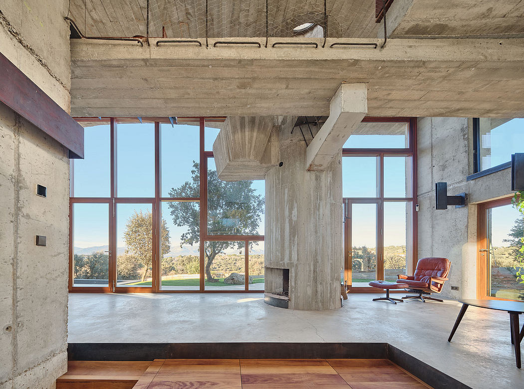 Modernist interior with concrete beams, large windows, and a wood-and-leather chair.