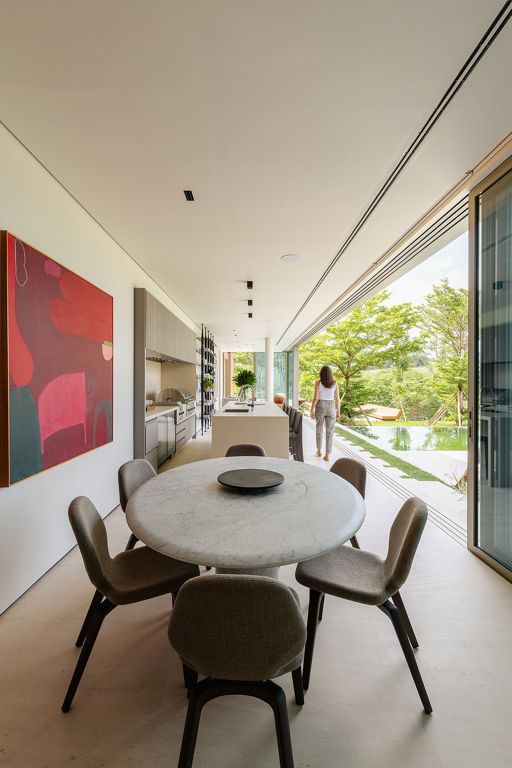 Spacious modern kitchen-dining area with large windows overlooking lush greenery.