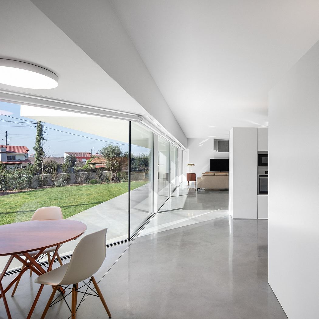 Open-concept interior with minimalist furniture, large glass doors, and a lush outdoor view.