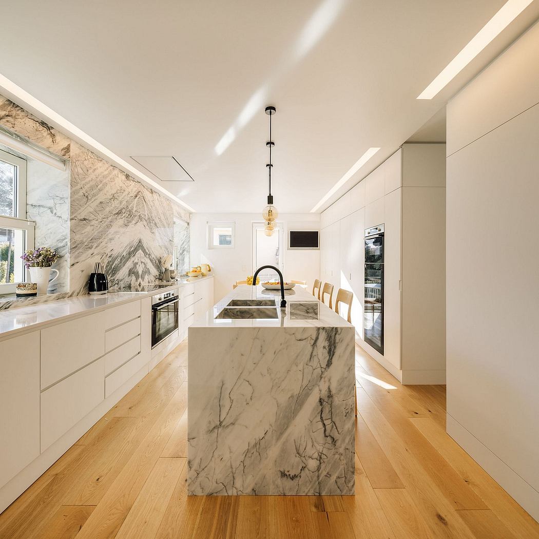 Spacious, modern kitchen with sleek cabinetry, marble island, and minimalist lighting.