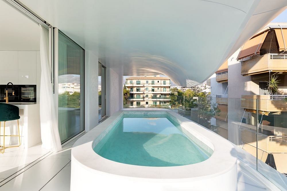 Modern pool area with curved glass walls, open-plan interior, and city skyline view.