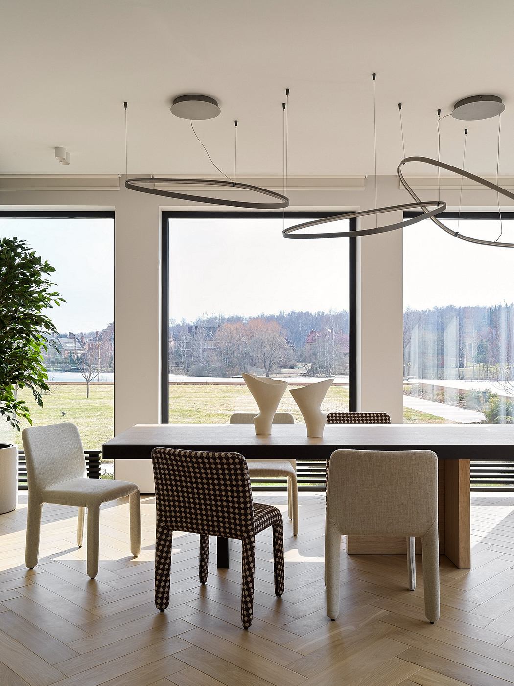 Minimalist dining room with modern lighting fixtures, wooden table, and patterned chairs.