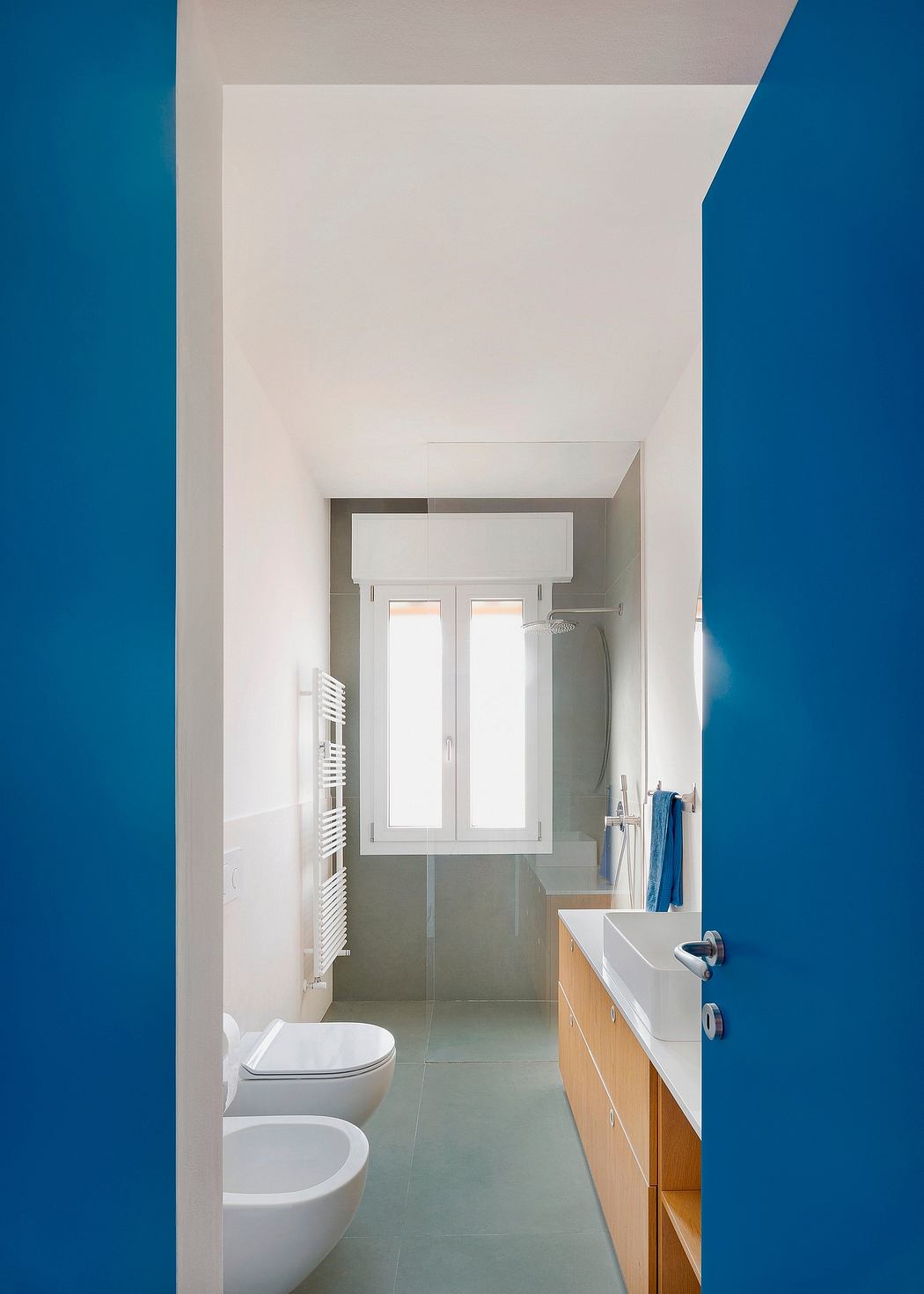 A modern bathroom with a white vanity, grey floor tiles, and a large window providing ample natural light.