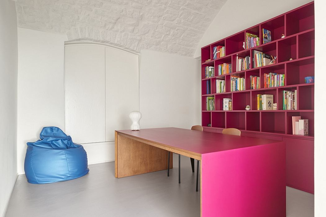 A minimalist, colorful home office with a striking red bookshelf and modern furnishings.