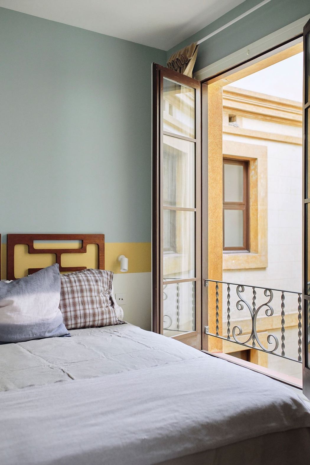 A cozy bedroom with a wooden headboard, patterned bedding, and a wrought-iron balcony.