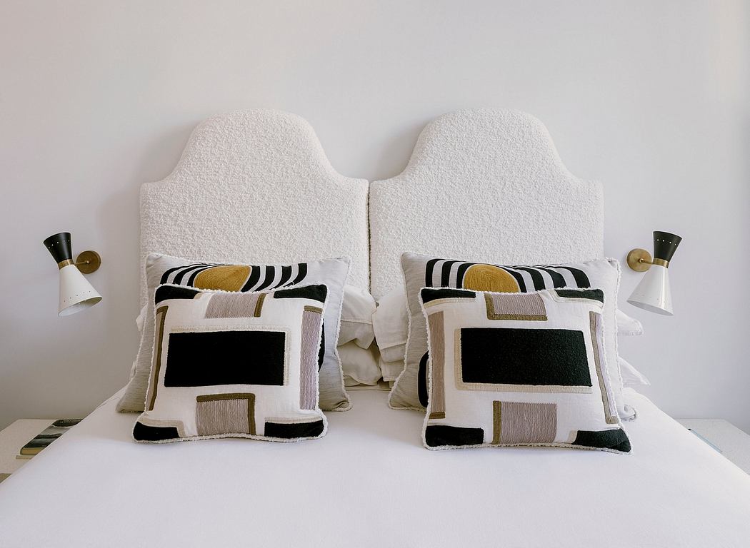 Twin headboards with abstract geometric patterned pillows and minimalist wall sconces.