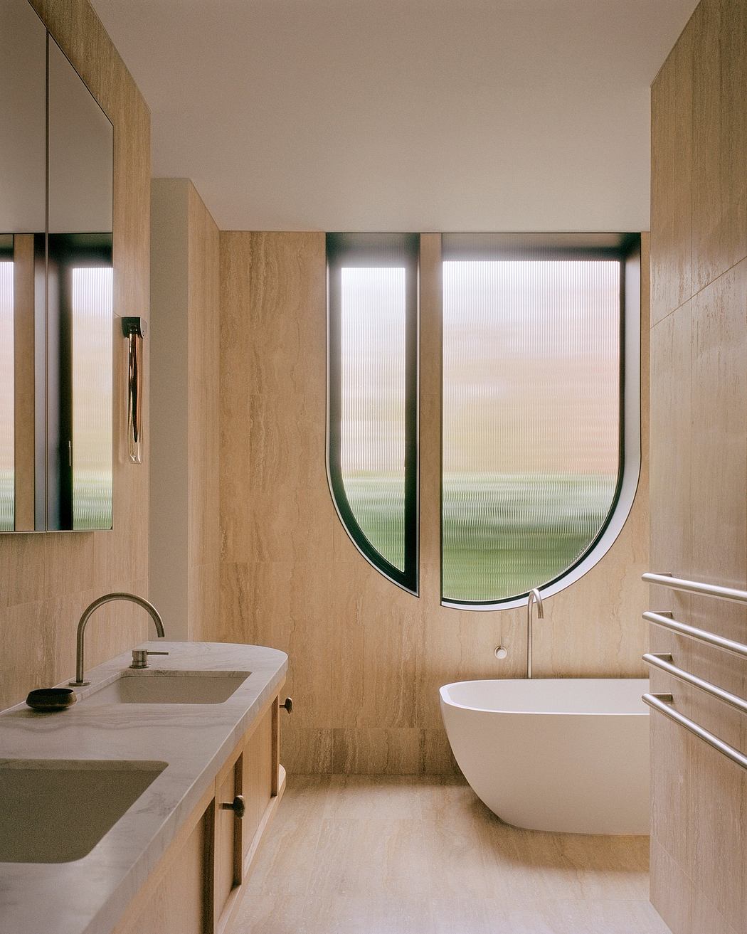 A modern bathroom with a curved window, travertine walls, and a freestanding bathtub.