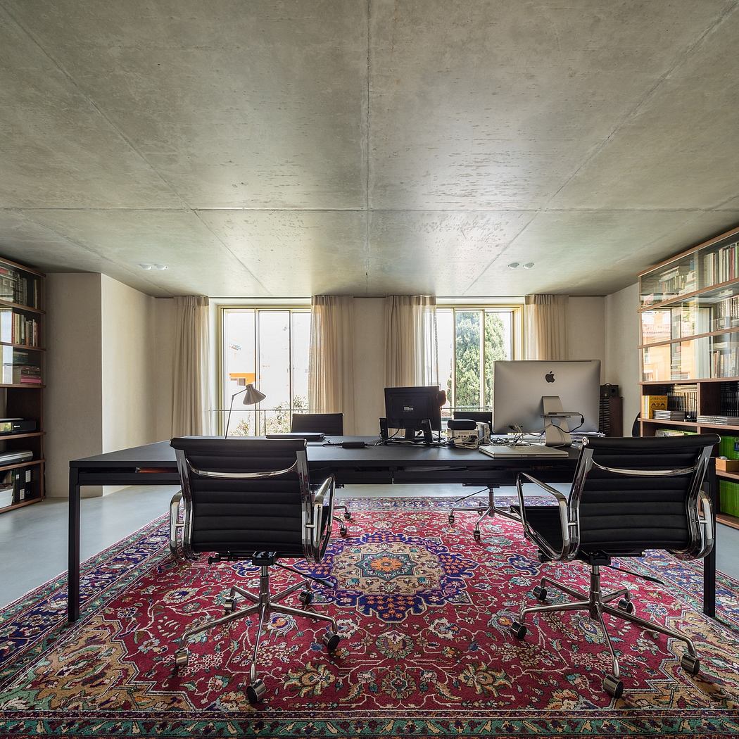 Spacious office with concrete ceiling, large windows, and vibrant patterned rug.