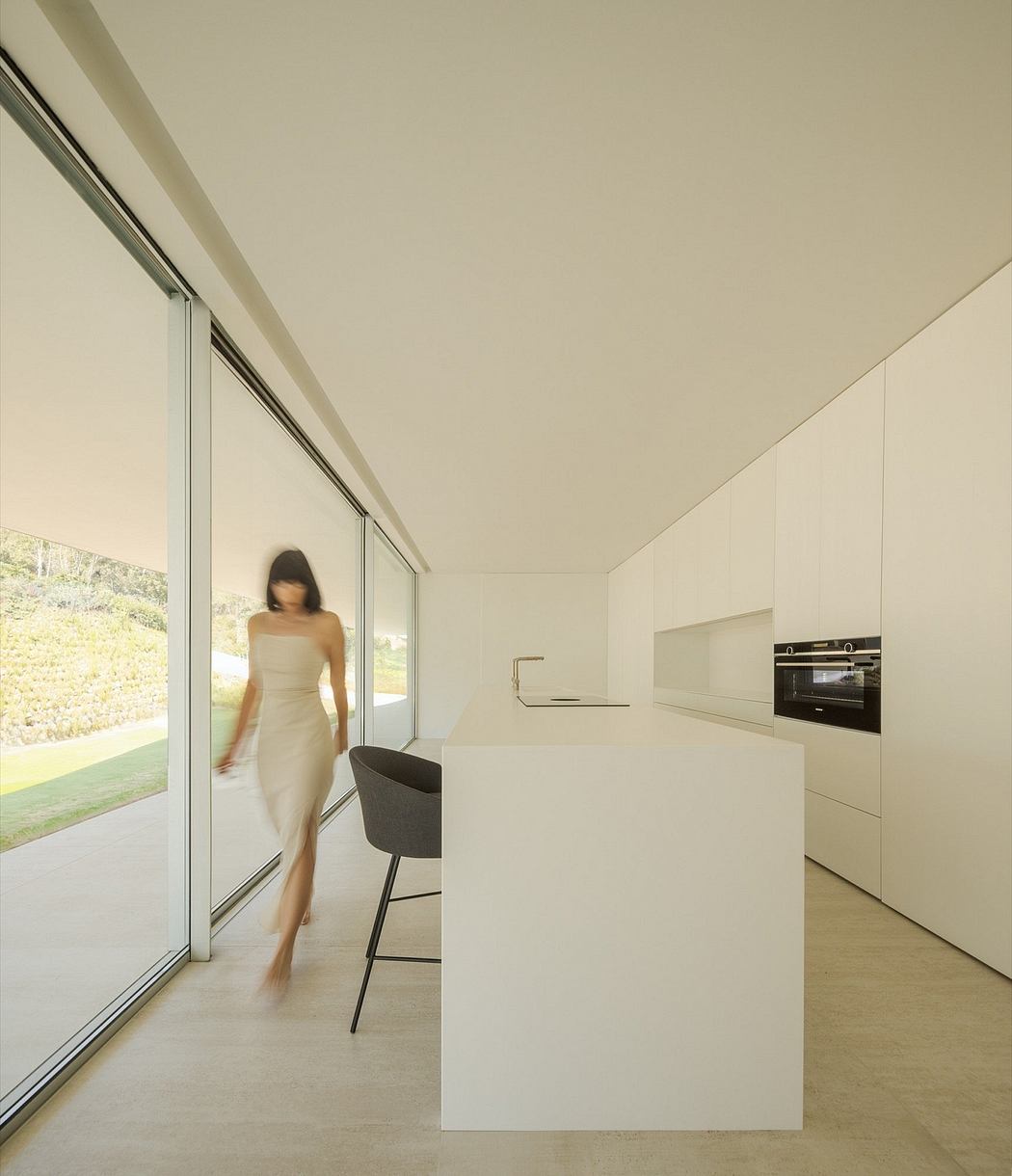 Minimalist interior with sleek kitchen, large windows, and a person moving through the space.