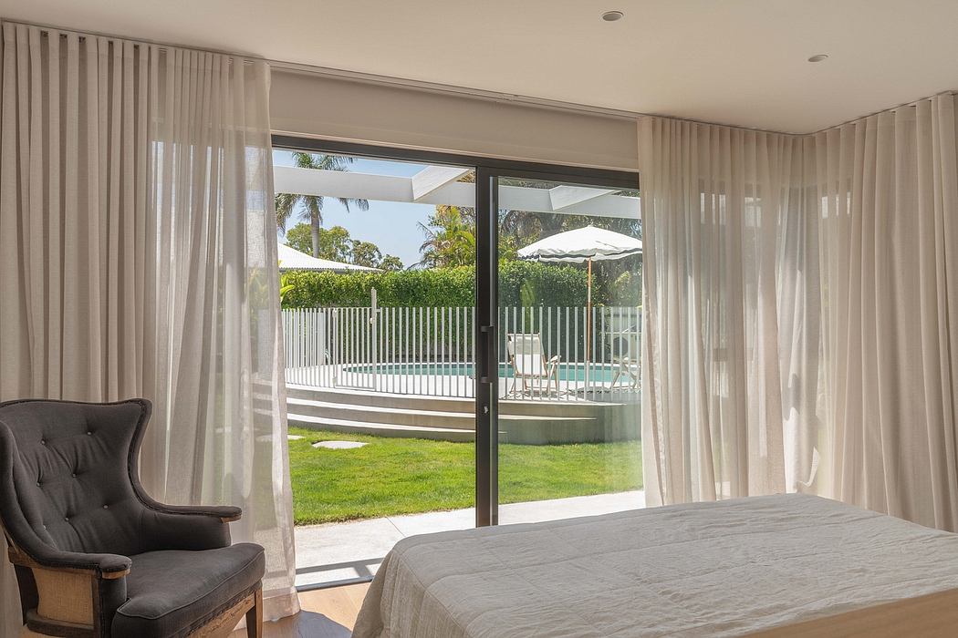 Spacious bedroom with floor-to-ceiling windows, curtains, and view of backyard patio.