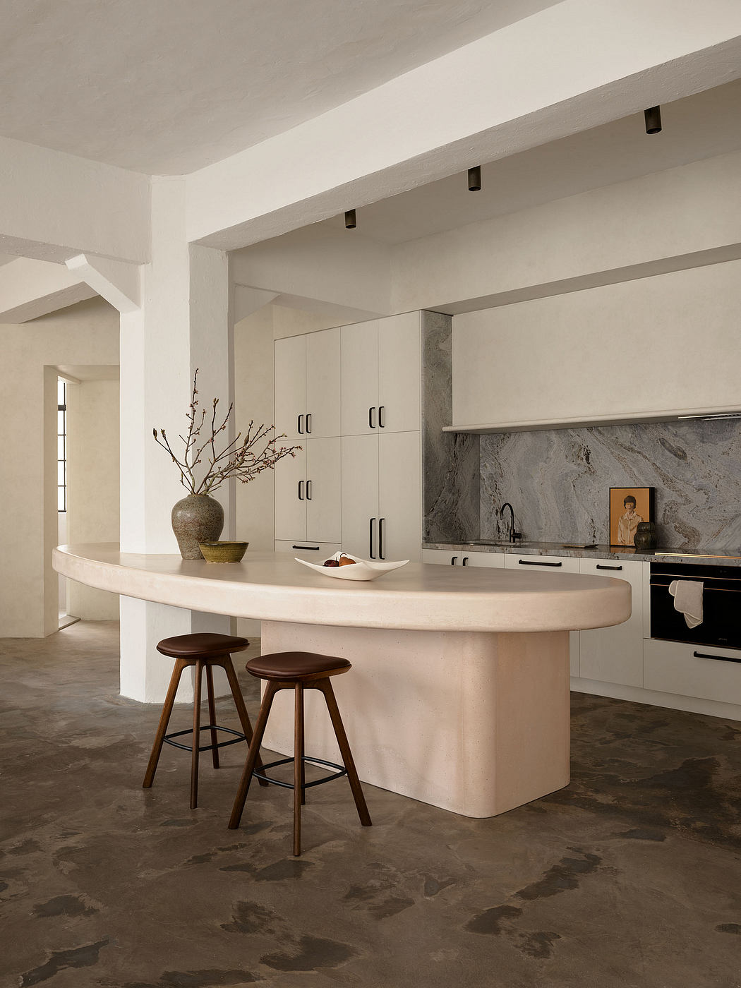 Sleek, minimalist kitchen with curved island, neutral color palette, and textured stone backsplash.