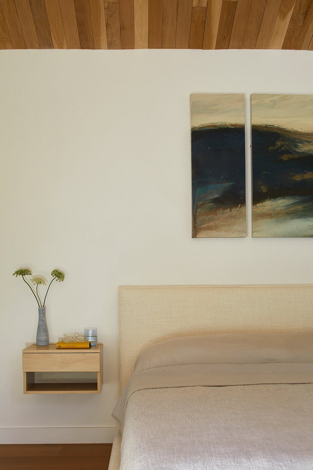 A cozy bedroom with minimalist decor, wood accents, and landscape artwork on the wall.