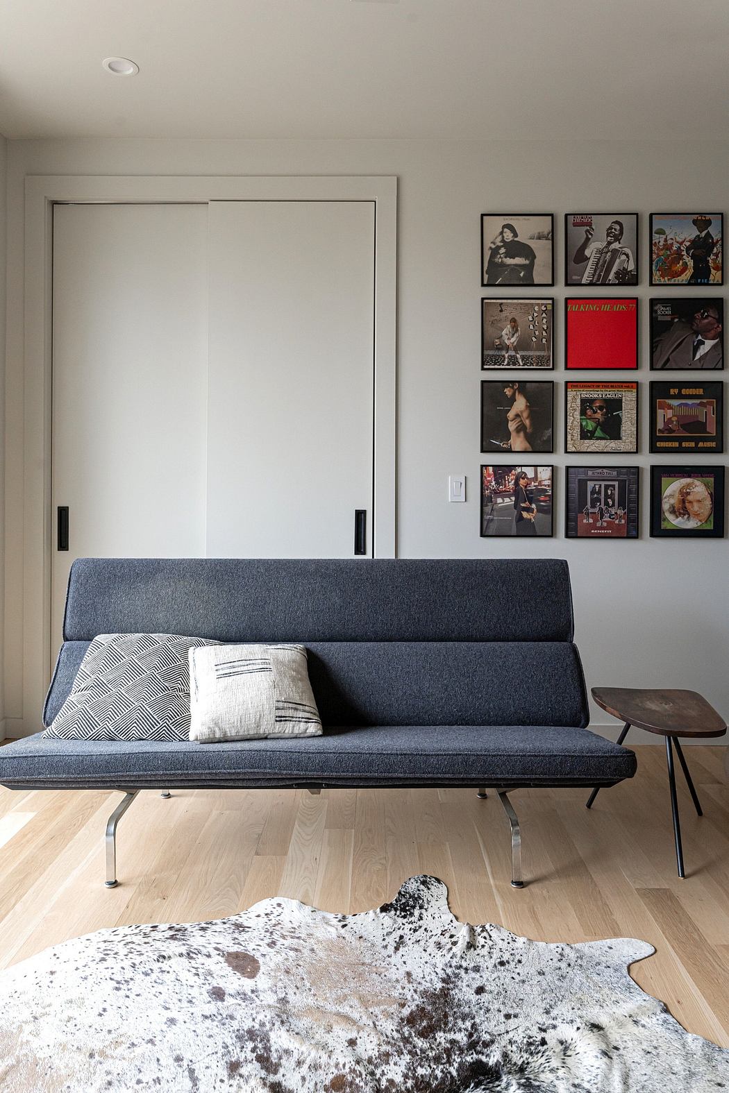 Modern living space with a sleek gray sofa, album cover art, and a patterned cowhide rug.