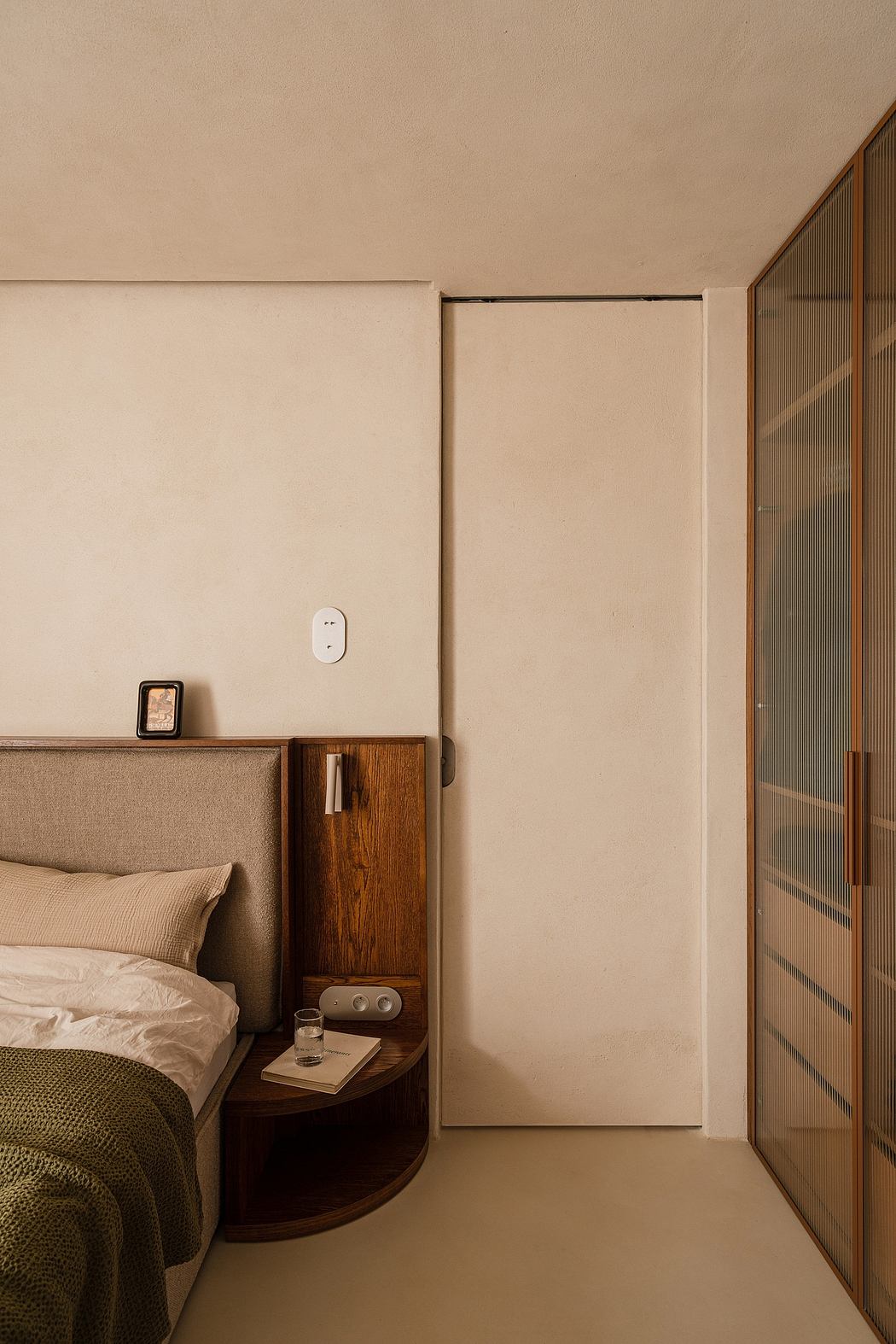 Minimalist bedroom with wood-paneled closet, bedside table, and neutral color scheme.