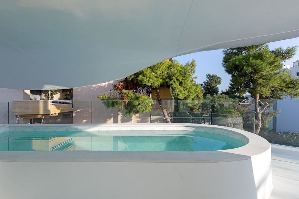 Modern, minimalist pool surrounded by glass walls and overlooking verdant landscape.