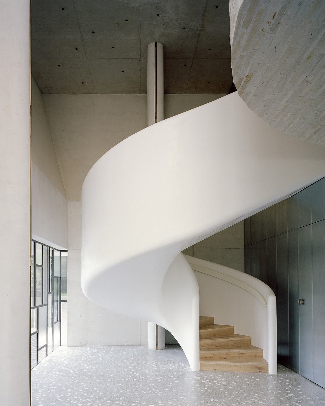 Curving white staircase with wooden steps leading up in an airy, minimalist interior.