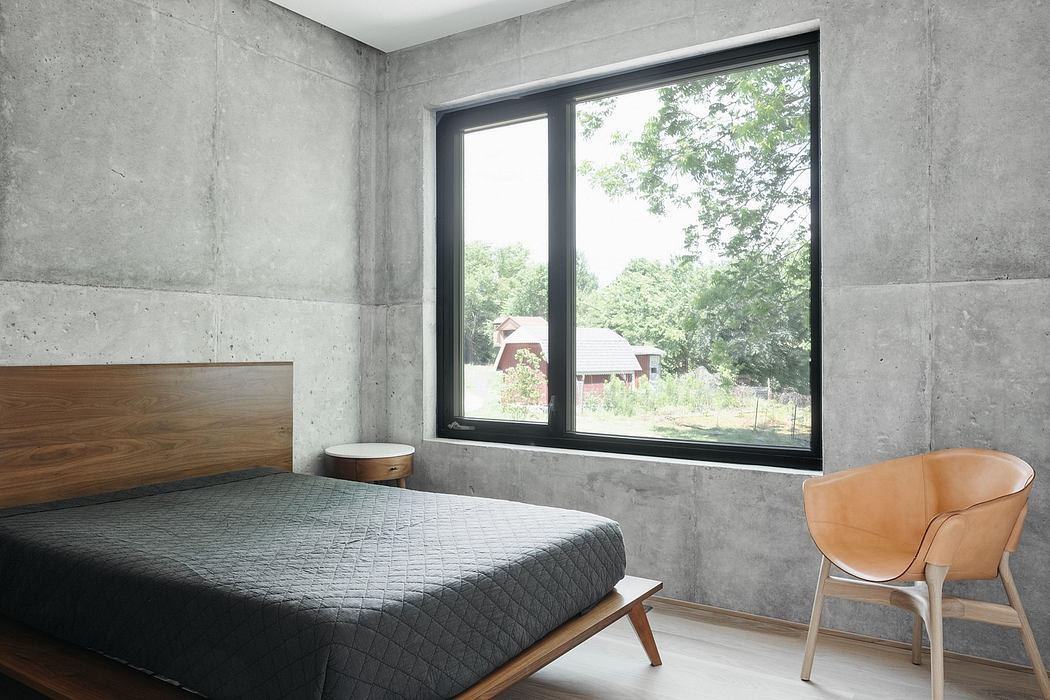 A modern, minimalist bedroom with concrete walls, large window, and wooden furniture.