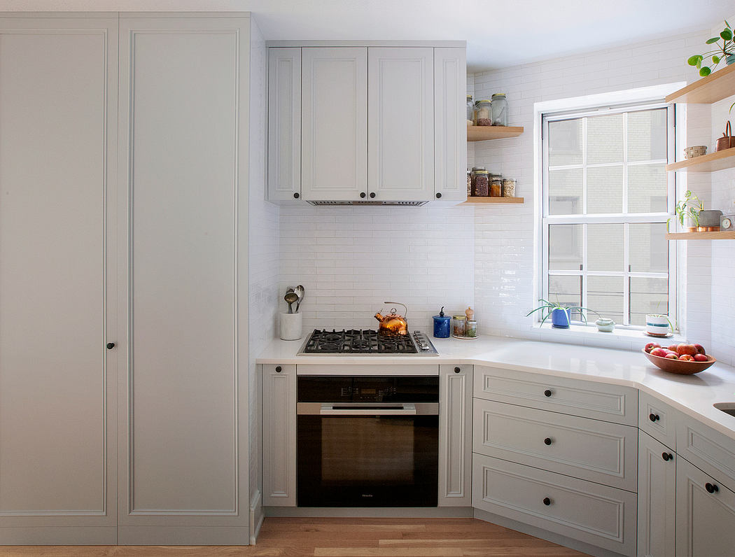 Cozy kitchen with light gray cabinetry, shelves, and gas stove under a window.
