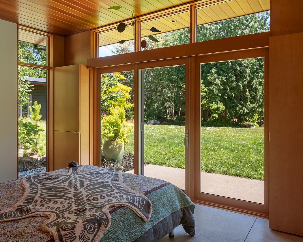Cozy bedroom with expansive windows overlooking a lush, verdant garden landscape.
