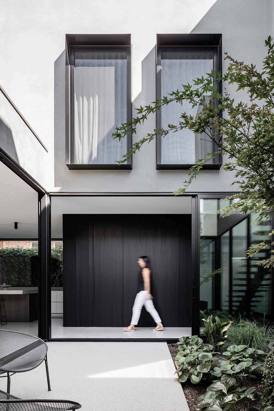 Sleek modern facade with slatted entry, large windows, and lush greenery accents.