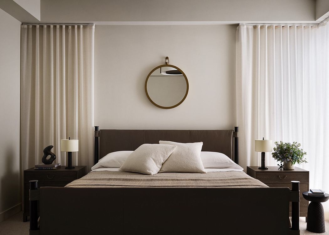 Modern bedroom with sleek dark furniture, circular mirror, and plush bedding.