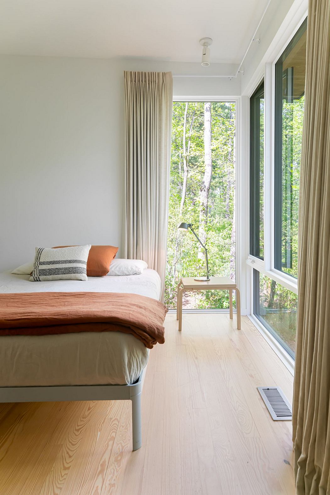 Bright, airy bedroom with large windows overlooking lush greenery and wood furnishings.