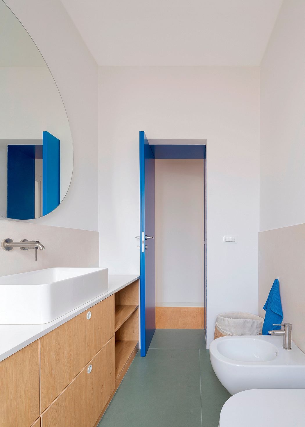 A modern bathroom with a vanity, sink, and mirror. The room features clean lines, neutral tones, and pops of blue.