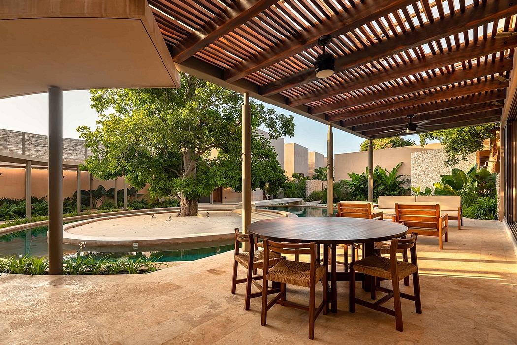 Rustic covered patio with round dining table, chairs, and a swimming pool surrounded by lush greenery.