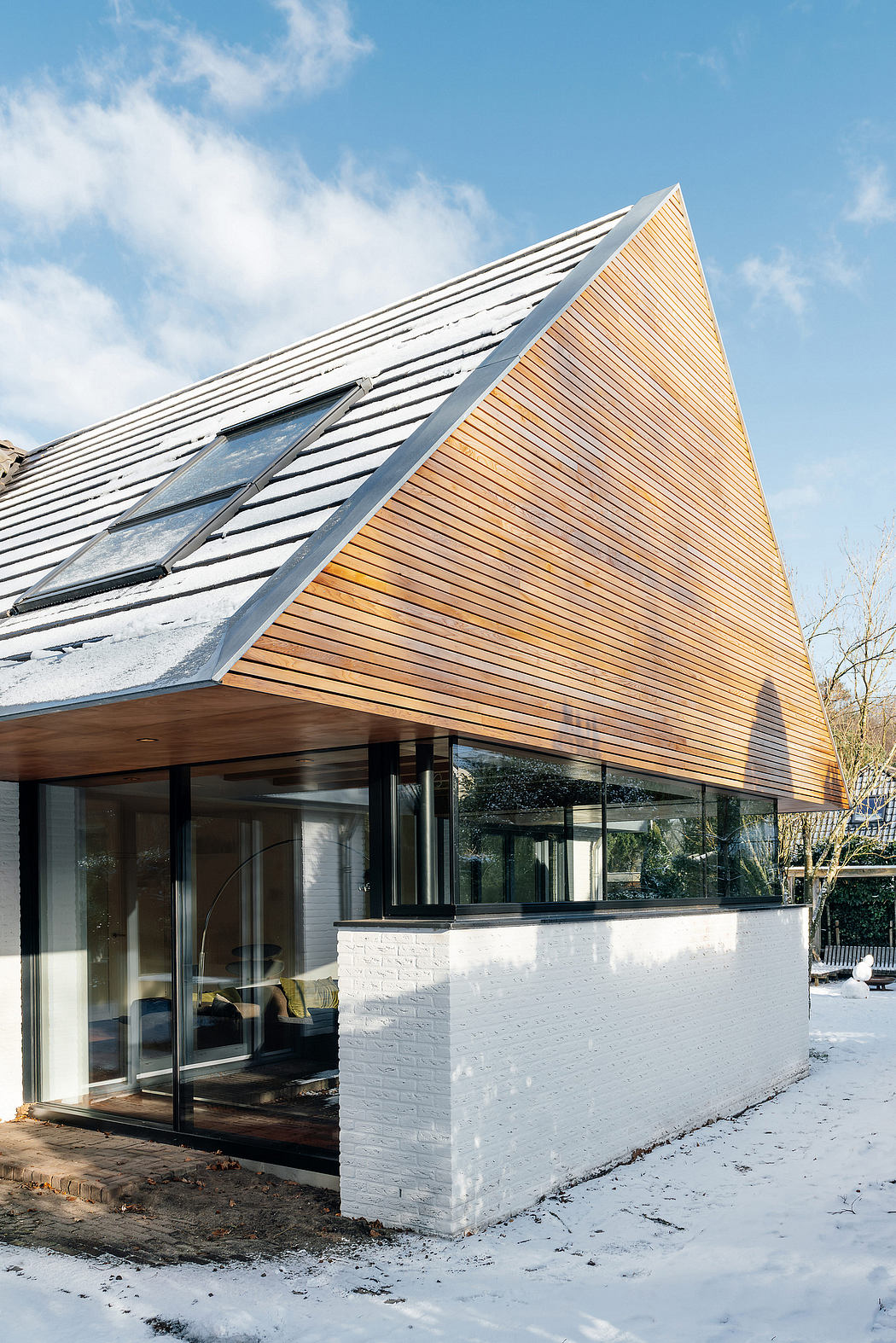 A modern architectural design with a striking triangular roof and contrasting wood and white brick facade.