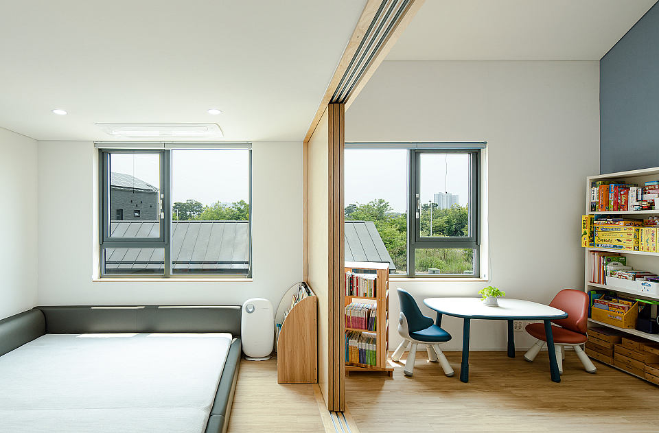 A modern, bright living space with geometric window frames, built-in shelving, and cozy furniture.